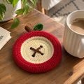 Apple Slice crochet coaster with cream center and red border beside a mug