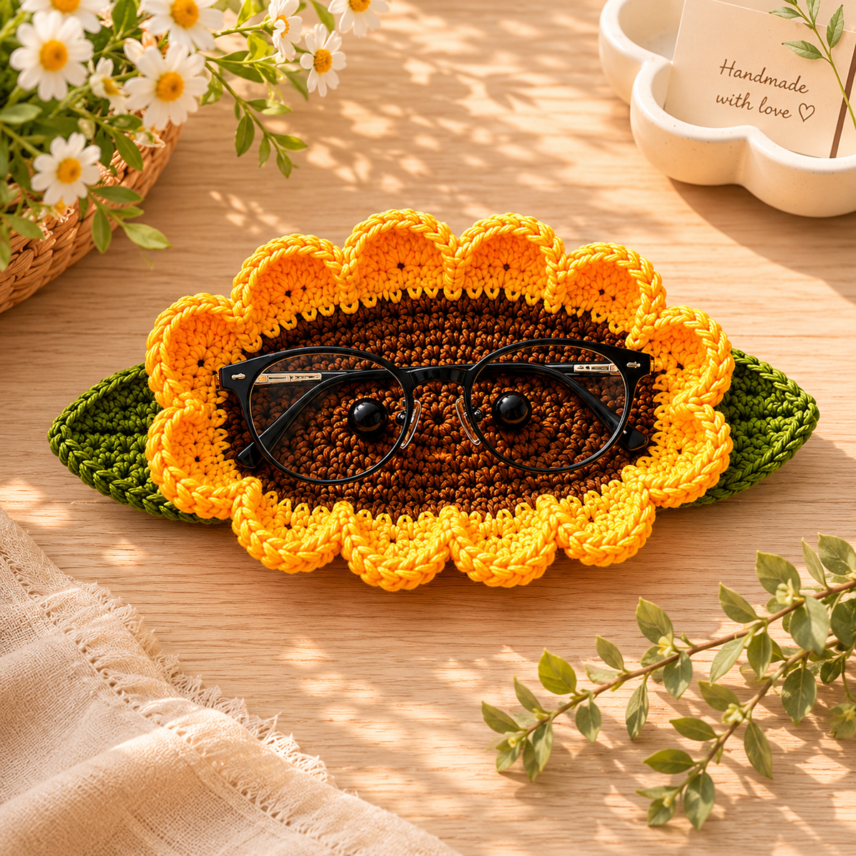 Handmade crochet glasses holder in a sunflower-inspired design with bright yellow petals and green leaf accents, displayed on a tabletop.